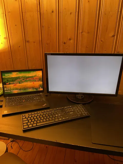 The creator’s desk: a used laptop and a monitor on a table in a wood-panelled basement.